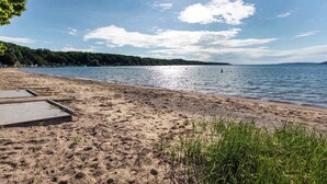 Ein Sandstrand mit einer Holzterrasse und freiem Blick auf den See.