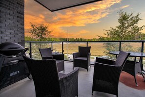 A balcony with wicker furniture, a grill, and a view of a sunset over a landscape.