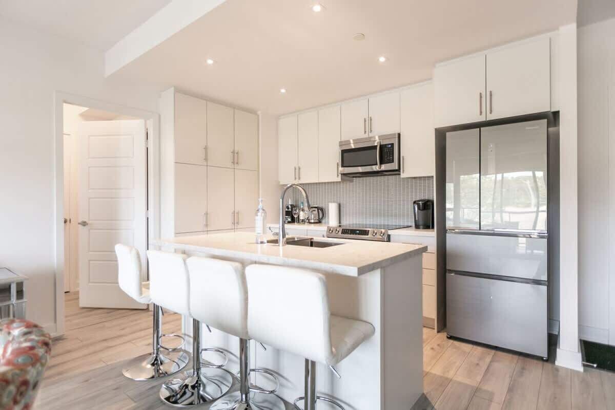 A modern kitchen with white cabinetry, stainless steel appliances, and a bar area with stools.