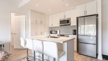 A modern kitchen with white cabinetry, stainless steel appliances, and a bar area with stools.