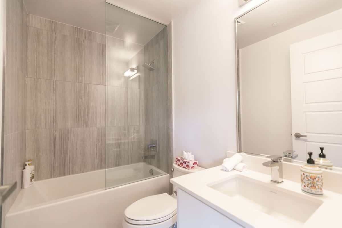 A modern bathroom with a glass-enclosed shower, a white toilet, and a sink with a mirror.
