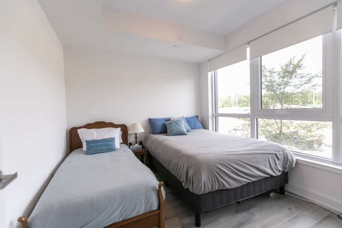 A bedroom with two beds, large windows, and a view of trees.