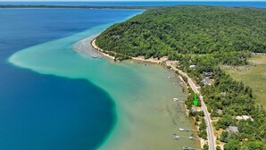 An aerial view of a coastal area with a clear blue sea, a curved shoreline, and a densely forested hill.