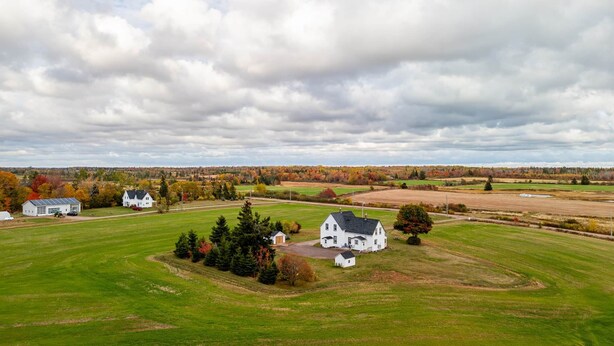 A rural landscape with a large white house surrounded by fields and trees. - Historic PEI Cottage with Modern Comforts, Riverside Views & Family-Friendly Fun (Prince Edward Island)