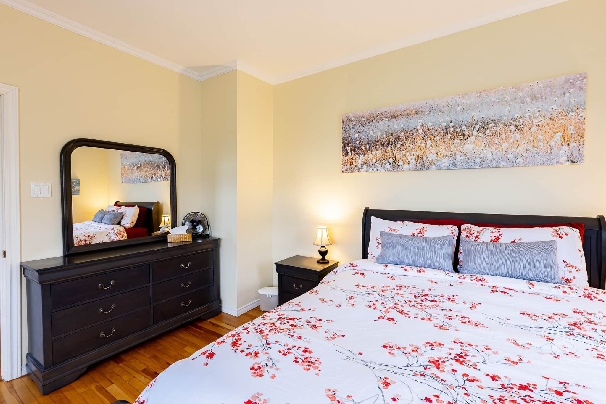Un dormitorio con cama, cómoda, mesita de noche y un cuadro abstracto grande en la pared.
