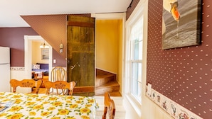 A bedroom with a bed, wooden chairs, a staircase, and a window with a view. - Historic PEI Cottage with Modern Comforts, Riverside Views & Family-Friendly Fun (Prince Edward Island)
