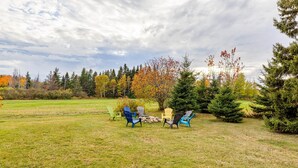 A grassy outdoor area with Adirondack chairs arranged around a fire pit. - Historic PEI Cottage with Modern Comforts, Riverside Views & Family-Friendly Fun (Prince Edward Island)
