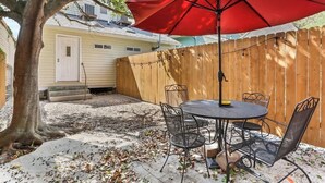 A patio with a round table and chairs, a red umbrella, and a wooden fence. - Beautiful Bywater Retreat with Private Patio (New Orleans)