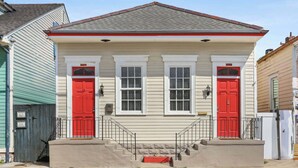 A two-story house with a beige facade, red doors, and a small front porch with steps. - Beautiful Bywater Retreat with Private Patio (New Orleans)