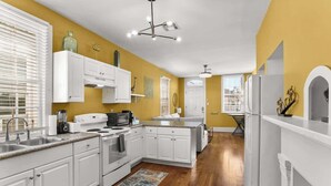 A modern kitchen with white cabinetry, a central island, and a view to the living area. - Beautiful Bywater Retreat with Private Patio (New Orleans)