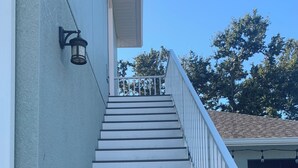 Eine Treppe mit weißen Stufen und einem weißen Geländer, die zu einem überdachten Veranda-Bereich führt.