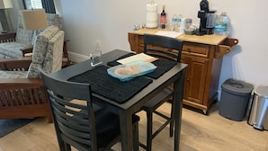Ein Essbereich mit Tisch für zwei Personen, einer Kaffeemaschine und einem Mülleimer.