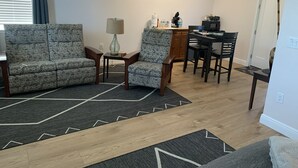 Ein Wohnzimmer mit einer Couch, Sesseln, einem Couchtisch, einem Esstisch mit Stühlen und einer Küchenzeile mit Mikrowelle und Schränken.