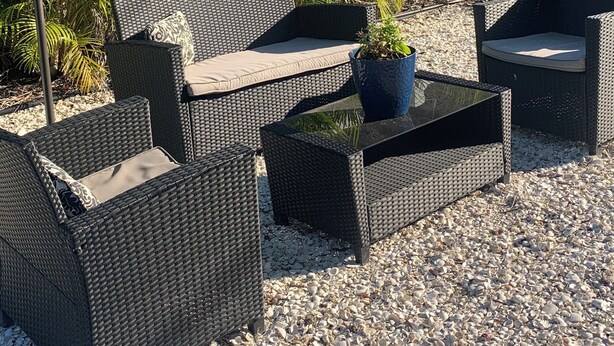 Gartenmöbel aus Rattan mit Kissen, ein Tisch mit Topfpflanze und ein grüner Sonnenschirm.