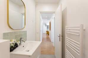 A modern bathroom with a white sink, a mirror, and a wooden floor. - Family Suite - Finlay (Paris)