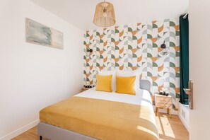 A modern bedroom with a bed, a bedside table, a wall-mounted lamp, and a geometric-patterned wall. - Family Suite - Finlay (Paris)