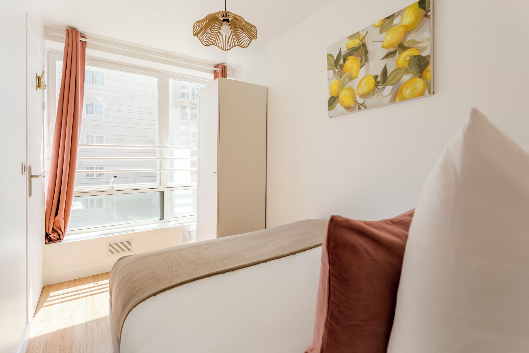 Une chambre à coucher avec un lit, une fenêtre avec des rideaux, un luminaire au plafond et un mur orné d’une œuvre d’art représentant des citrons.
