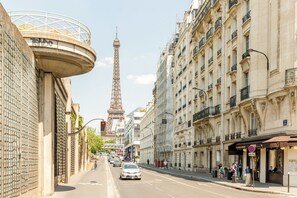 A street view with the Eiffel Tower in the background, buildings with balconies, and a café on the right. - Family Suite - Finlay (Paris)