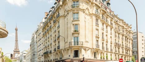 A historic building with ornate architecture, a prominent entrance, and a view of the Eiffel Tower in the background.