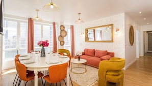 A modern living room with a dining area, featuring a round table, orange chairs, a red sofa, and a yellow armchair. - Family Suite - Finlay (Paris)