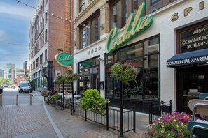 Une vue de rue d'un immeuble sur lequel on peut voir une enseigne « Cadillac », indiquant une zone commerciale avec des boutiques et des appartements.