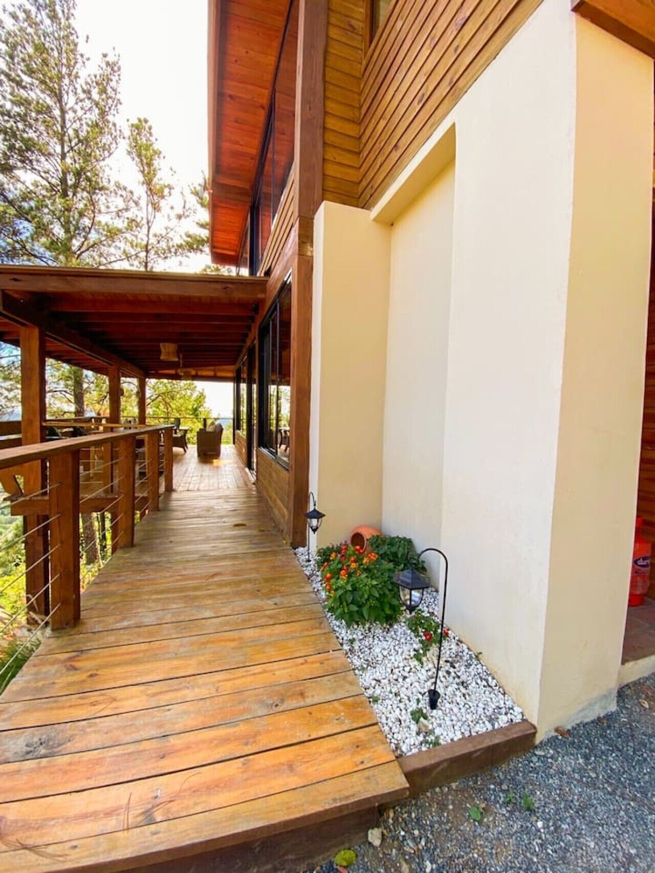 A wooden deck leading to a building with a covered porch and a small garden area with gravel and plants.