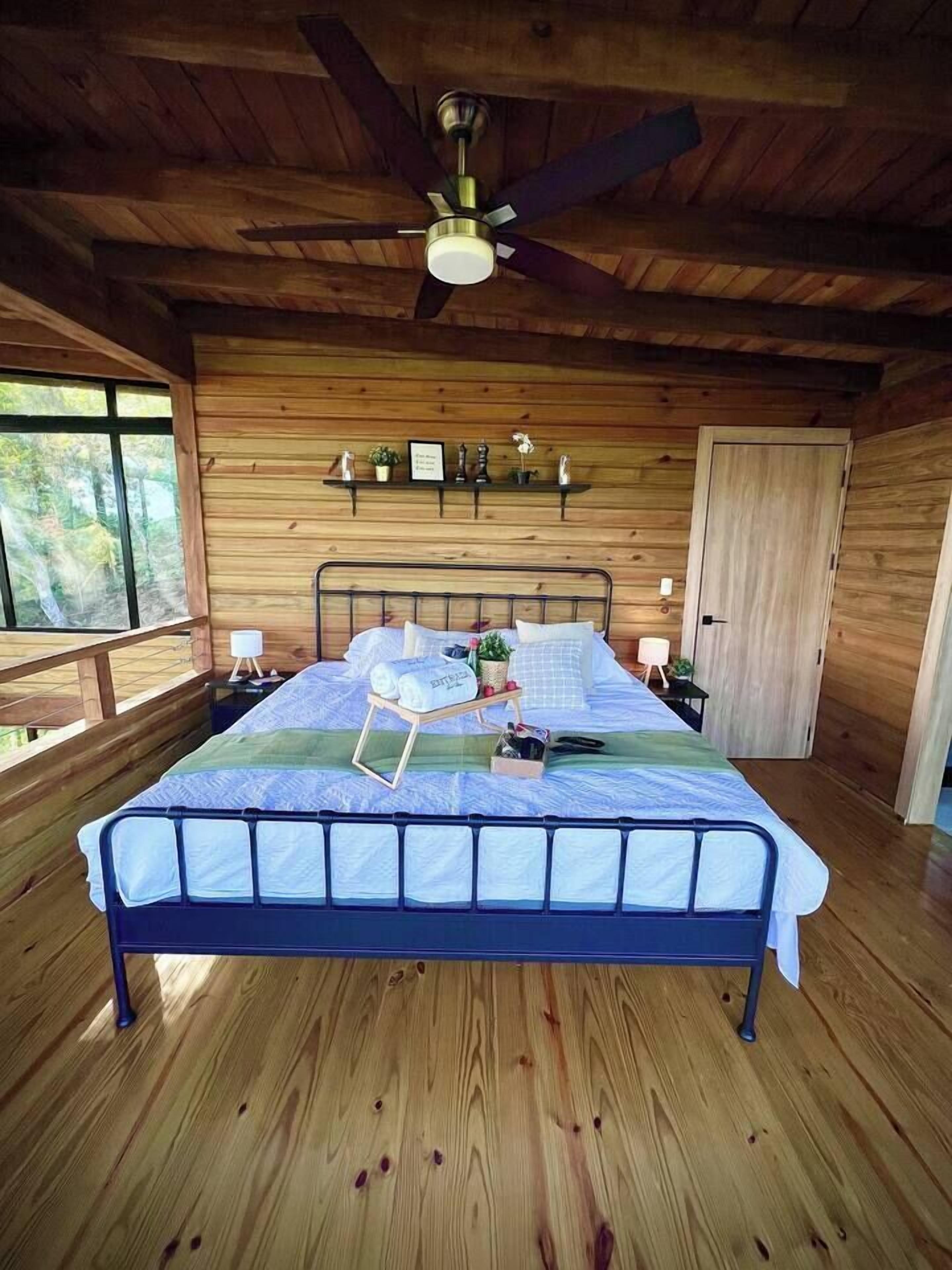 Une chambre dans une cabane en bois, avec un lit, un ventilateur de plafond et une fenêtre.