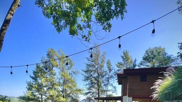 A hot tub with a clear view of the surrounding landscape, a wooden cabin, and string lights.