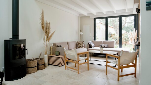 A living room with a fireplace, a sofa, two chairs, and a coffee table. There are baskets and pampas grass on the floor.