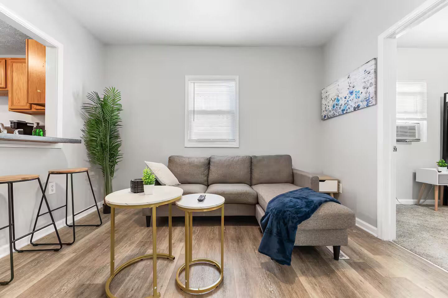 A compact living space with a kitchenette, a sofa, two small tables, and a large plant.
