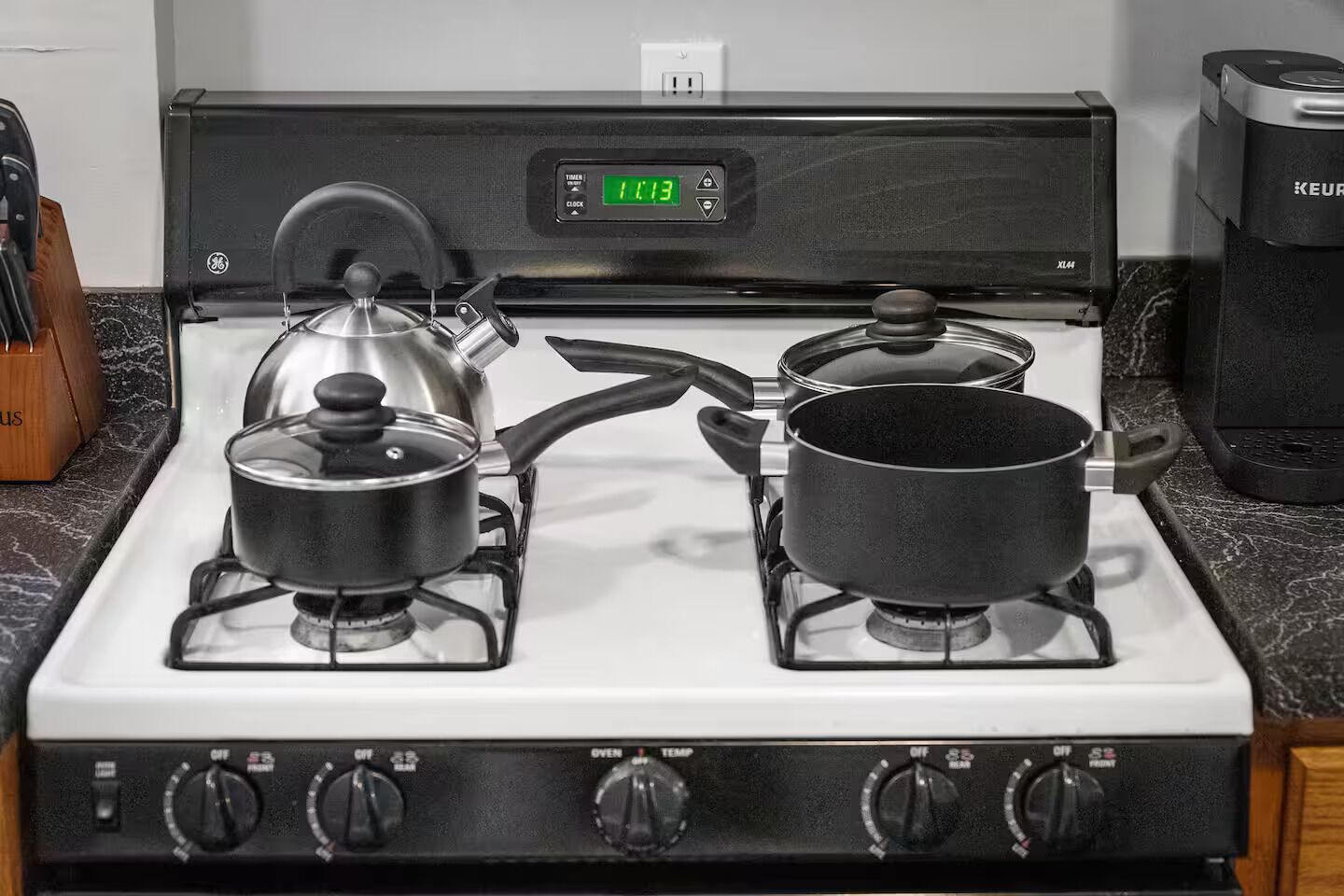 A kitchen with a stove, two pots, and a kettle.