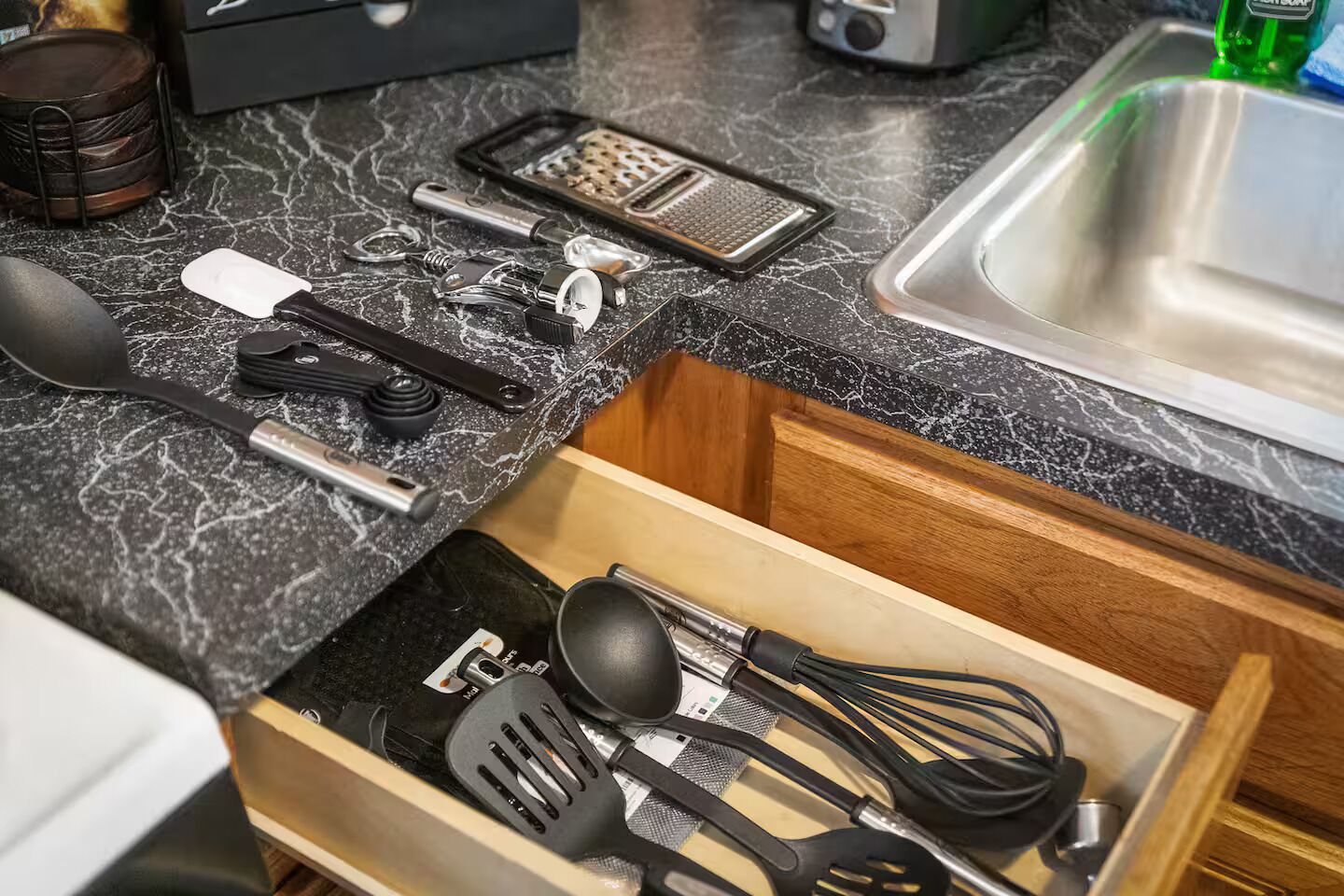 Una encimera de cocina con diversos utensilios y un cajón con herramientas de cocina.