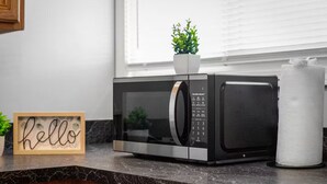 A kitchen with a microwave, a potted plant, and a sign that says "hello sunshine".
