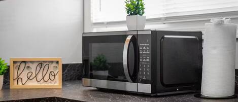 A kitchen with a microwave, a potted plant, and a sign that says "hello sunshine".