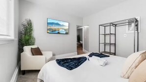 A bedroom with a bed, a chair, a TV, a plant, and a wardrobe.