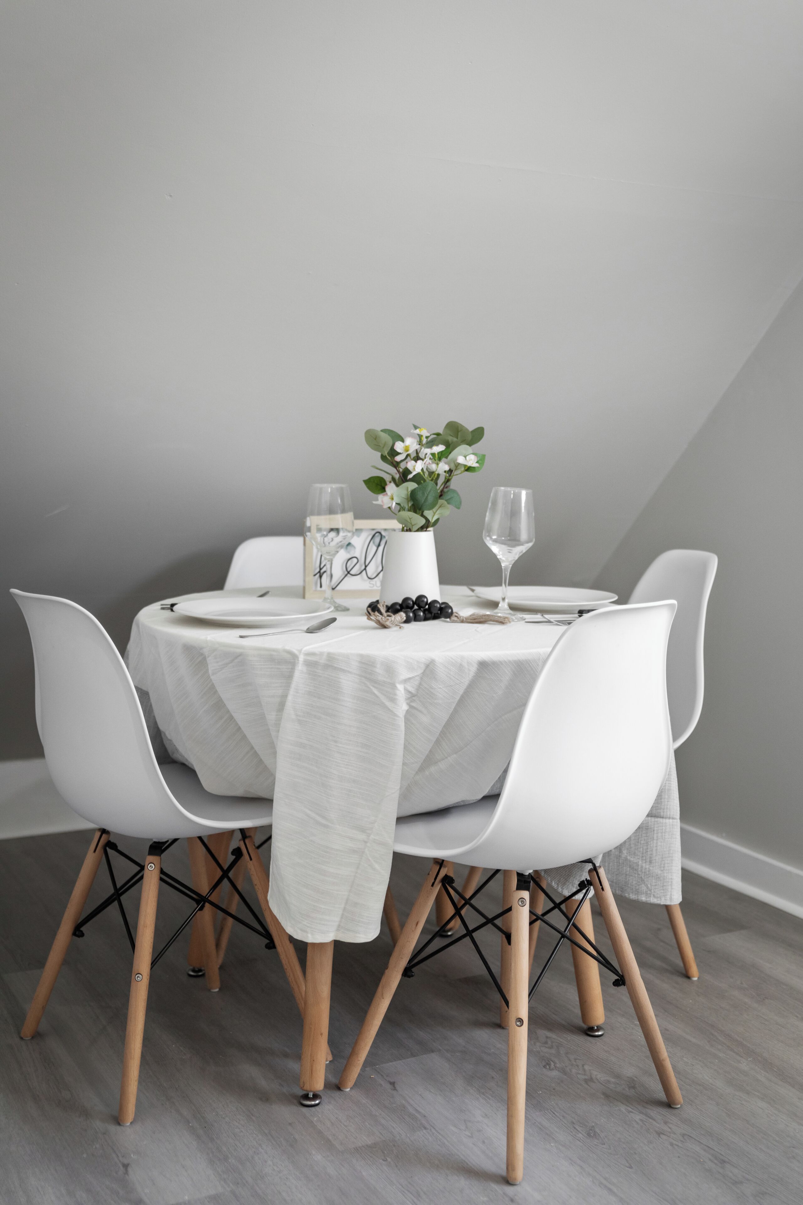 A dining table with white chairs, a vase with flowers, and a glass of water.