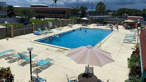 Ein Swimmingpool mit Liegestühlen und Sonnenschirmen, umgeben von einem Holzzaun und einem Gebäude im Hintergrund.