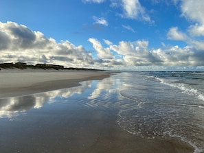 A beach with a wide sandy shore, gentle waves, and a clear sky with scattered clouds.