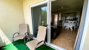 Ein Balkon mit zwei Stühlen und einem Tisch, eine Schiebeglastür, die in einen Essbereich mit Tisch und Stühlen führt, und ein Deckenventilator.
