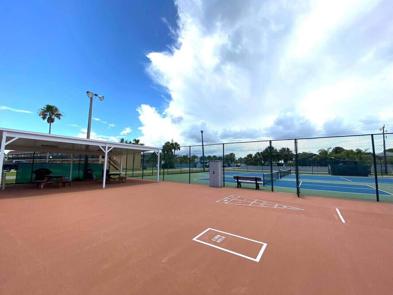 An outdoor tennis court with a covered seating area and a pavilion.