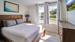 Un dormitorio con una cama grande, un cabecero de madera, una mesita de noche con lámpara, un aparador y una ventana con cortinas.