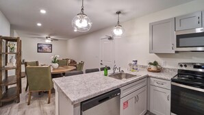 Una cocina moderna con encimeras de granito, electrodomésticos de acero inoxidable y un comedor con mesa y sillas de madera.