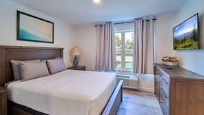 Une chambre à coucher avec un grand lit, une table de chevet, une commode, une lampe et un téléviseur.