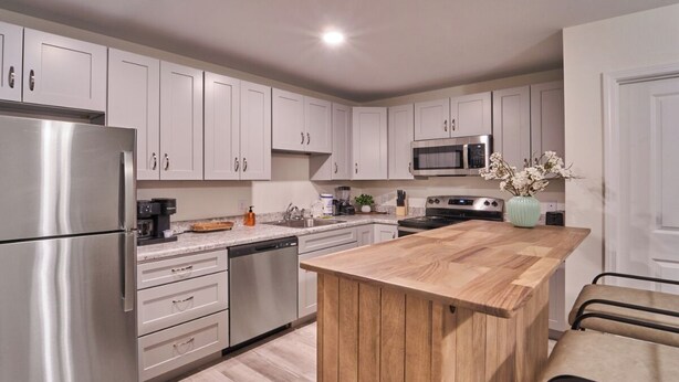 Una cocina moderna con gabinetes blancos, electrodomésticos de acero inoxidable y una isla de madera.