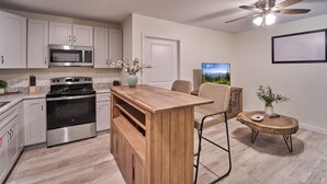 Una cocina moderna con electrodomésticos de acero inoxidable, una isla de madera y una zona de comedor con una silla y una mesita.