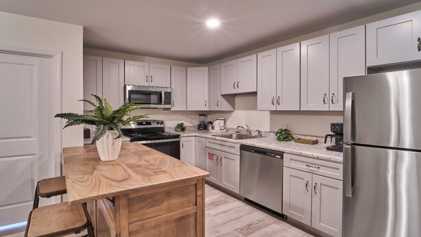A modern kitchen with white cabinets, stainless steel appliances, a wooden island, and bar stools. - Ruby 208: 1BD | Great LOCATION + Shared Amenities! (Pigeon Forge)