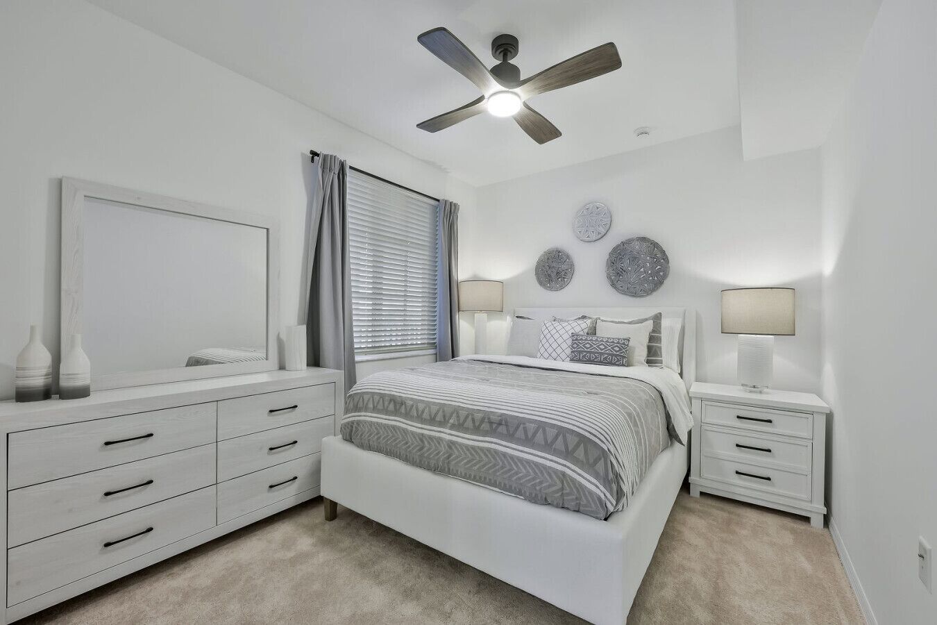 A bedroom with a bed, nightstands, a dresser, a ceiling fan, and decorative wall plates.