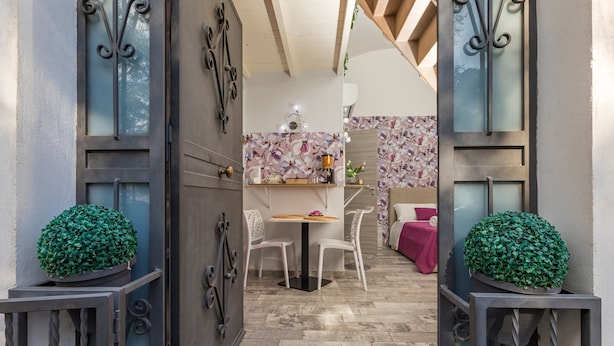 A doorway leading to a dining area with a table and chairs, a small kitchen area with a counter and decorative items, and a potted plant on the floor.