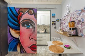 Une cuisine moderne équipée d’une machine à café, d’un mur décoratif orné de motifs floraux et d’un tableau représentant le visage d’une femme.