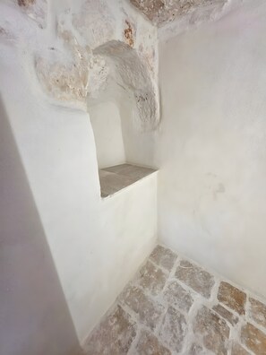 A room with a stone floor, white walls, and a small alcove with a stone ledge.